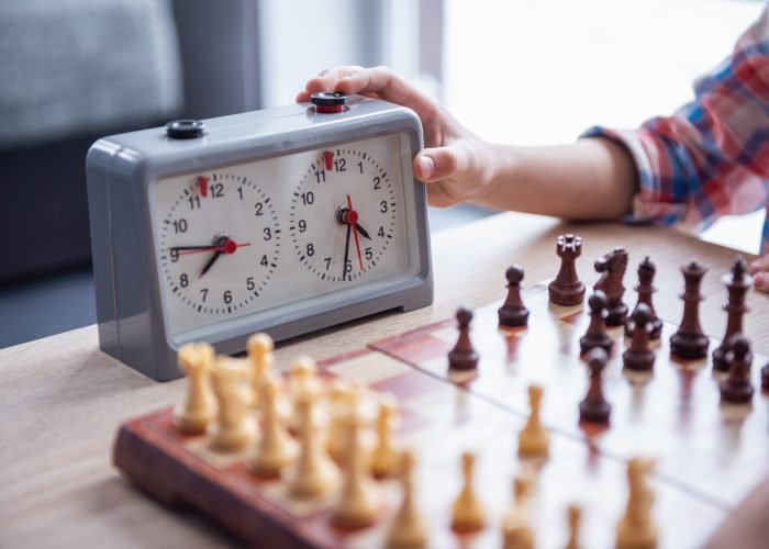 Cropped image of little boy playing chess, hand on timer